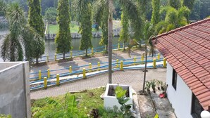 A view of a river with a bridge, surrounded by tall trees and a white building with a red roof. - Omahe Winahyu Homestay (Jogja)