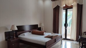 A hotel room with a bed, nightstand, lamp, and a view of the outdoors through a door. - Omahe Winahyu Homestay (Jogja)