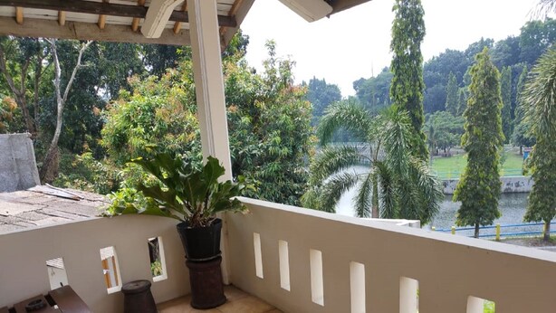 A balcony with a wooden bench, potted plants, and a view of a park with trees and a pathway. - Omahe Winahyu Homestay (Jogja)