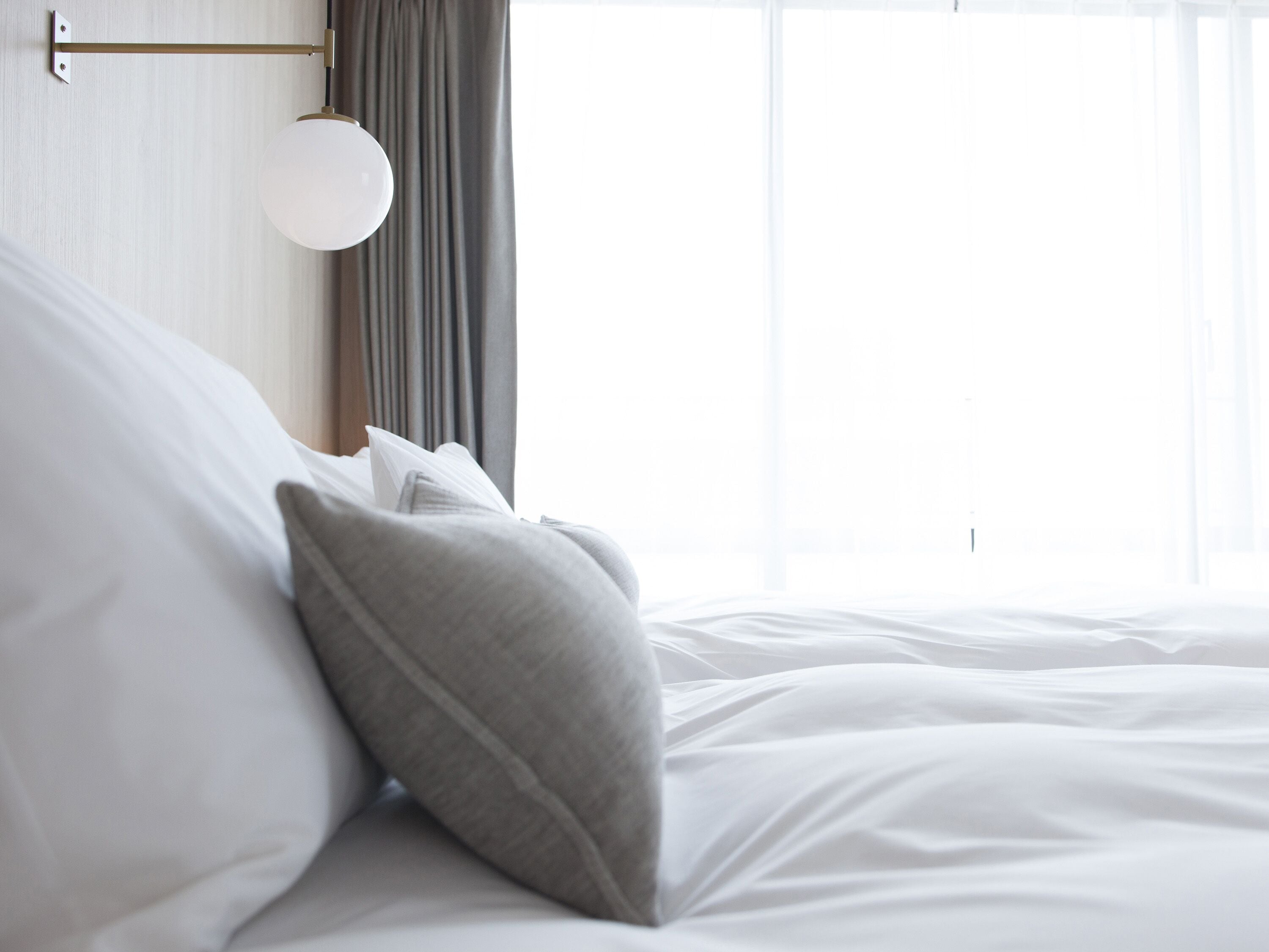 Una cama bien hecha con sábanas blancas y una almohada gris.