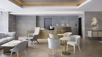 Een moderne hotellobby met een receptiebalie, een zithoek en een visgraatvloer.