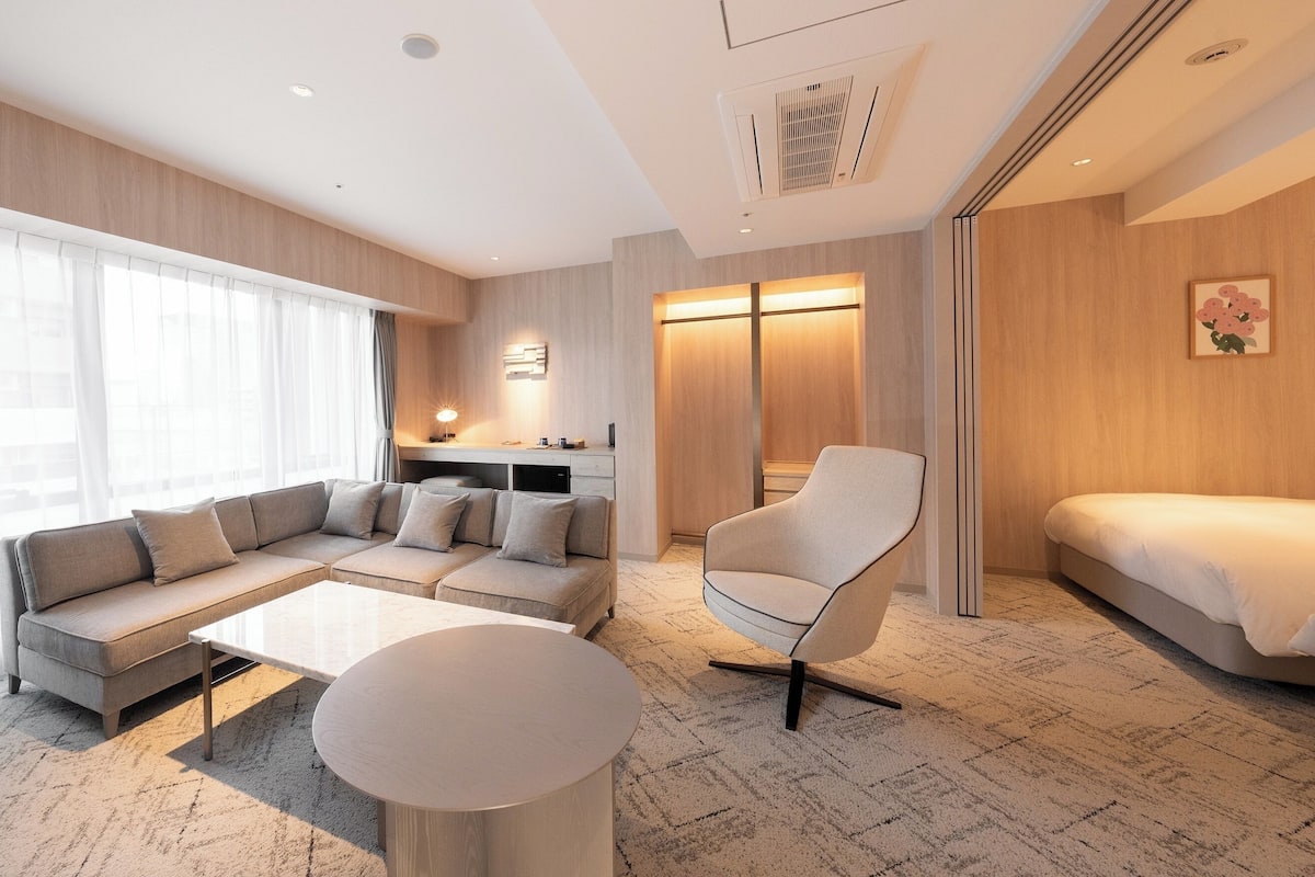 Quarto de hotel moderno com sofá, poltrona, cama e área de trabalho.