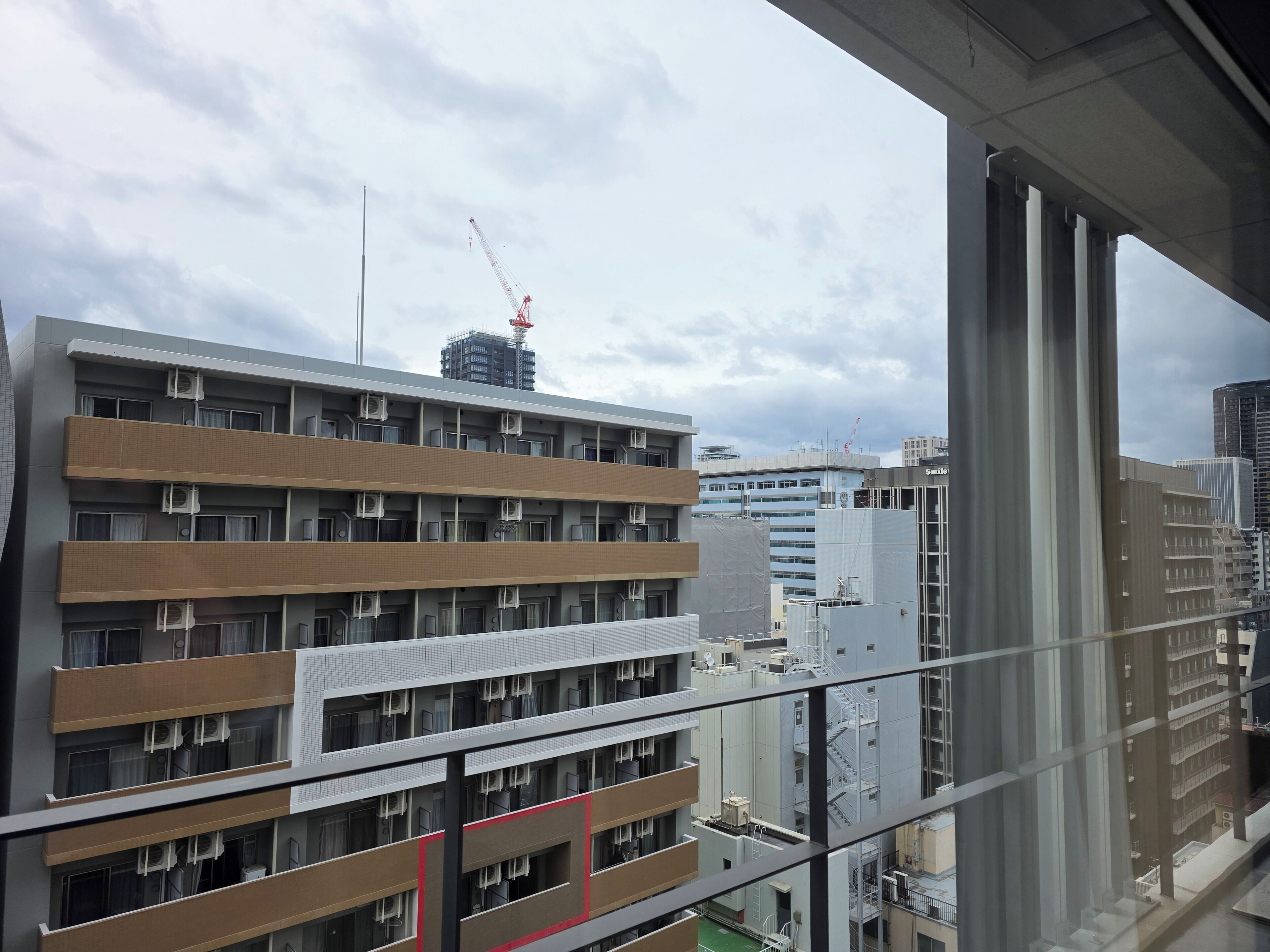 A multi-story building with balconies, air conditioning units, and a construction crane in the background.