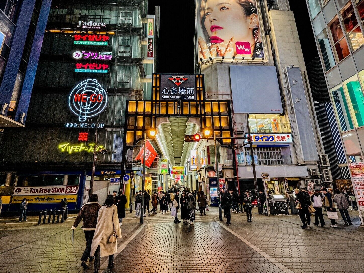 Una calle urbana concurrida por la noche, con letreros y escaparates iluminados.