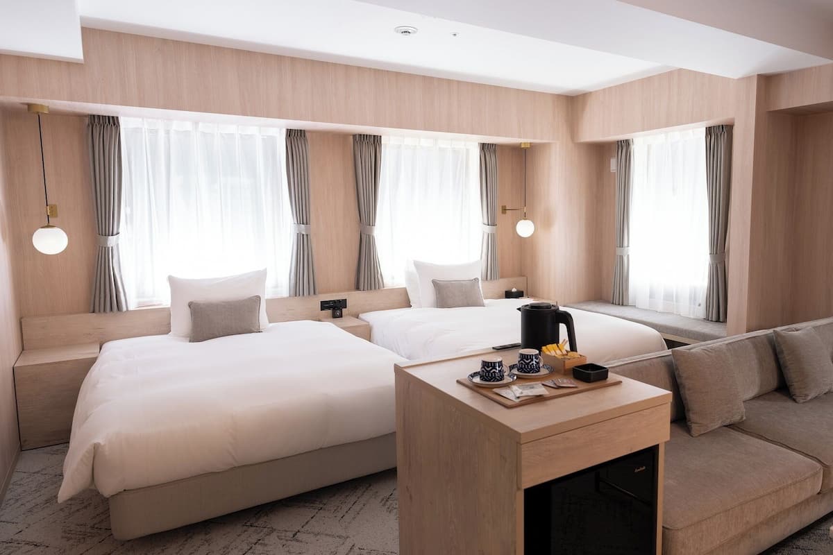 Quarto de hotel com duas camas, um sofá, uma mesa de centro e vista para a cidade.