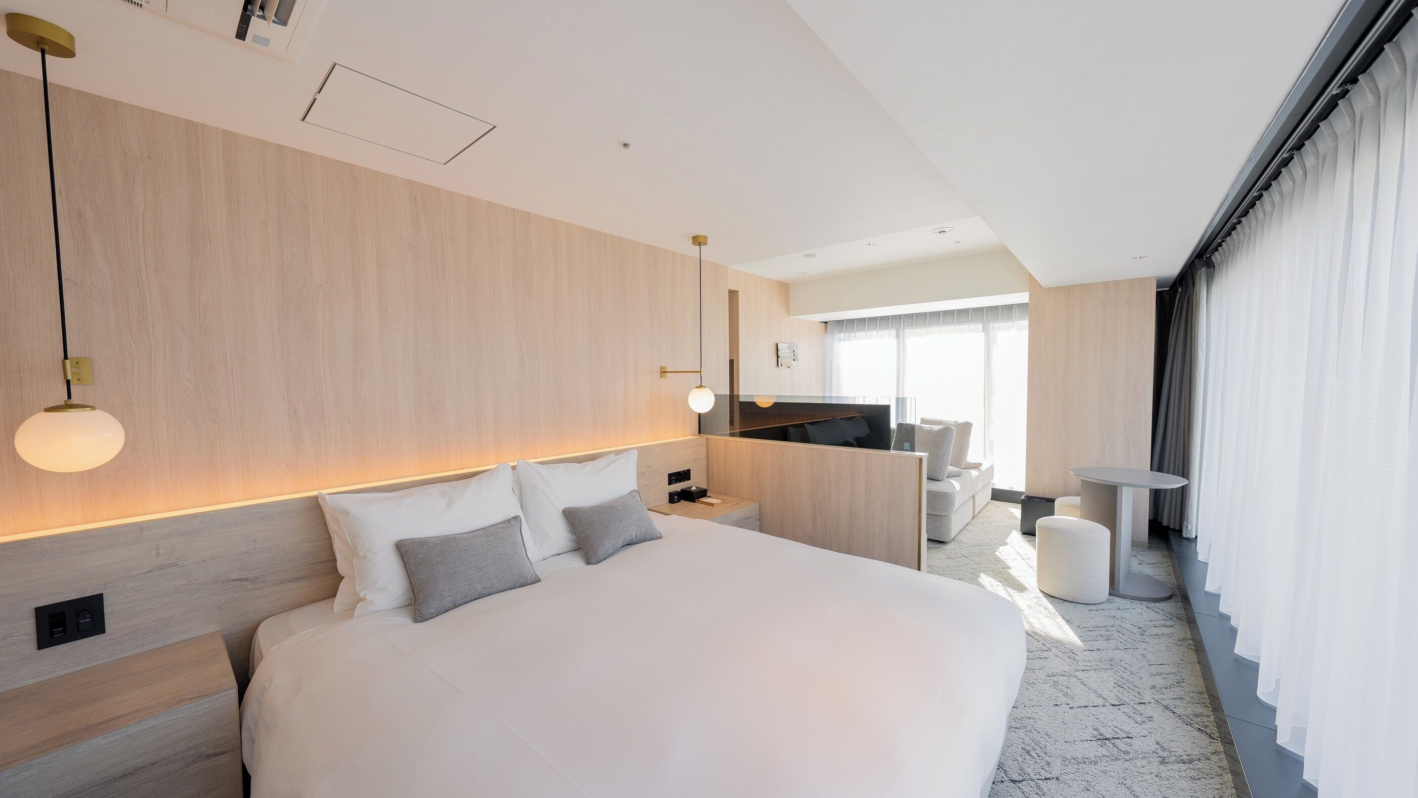 Un cuarto de hotel moderno con una cama grande, mesitas de noche, un escritorio, una silla y vista a la cocina y el área de estar.