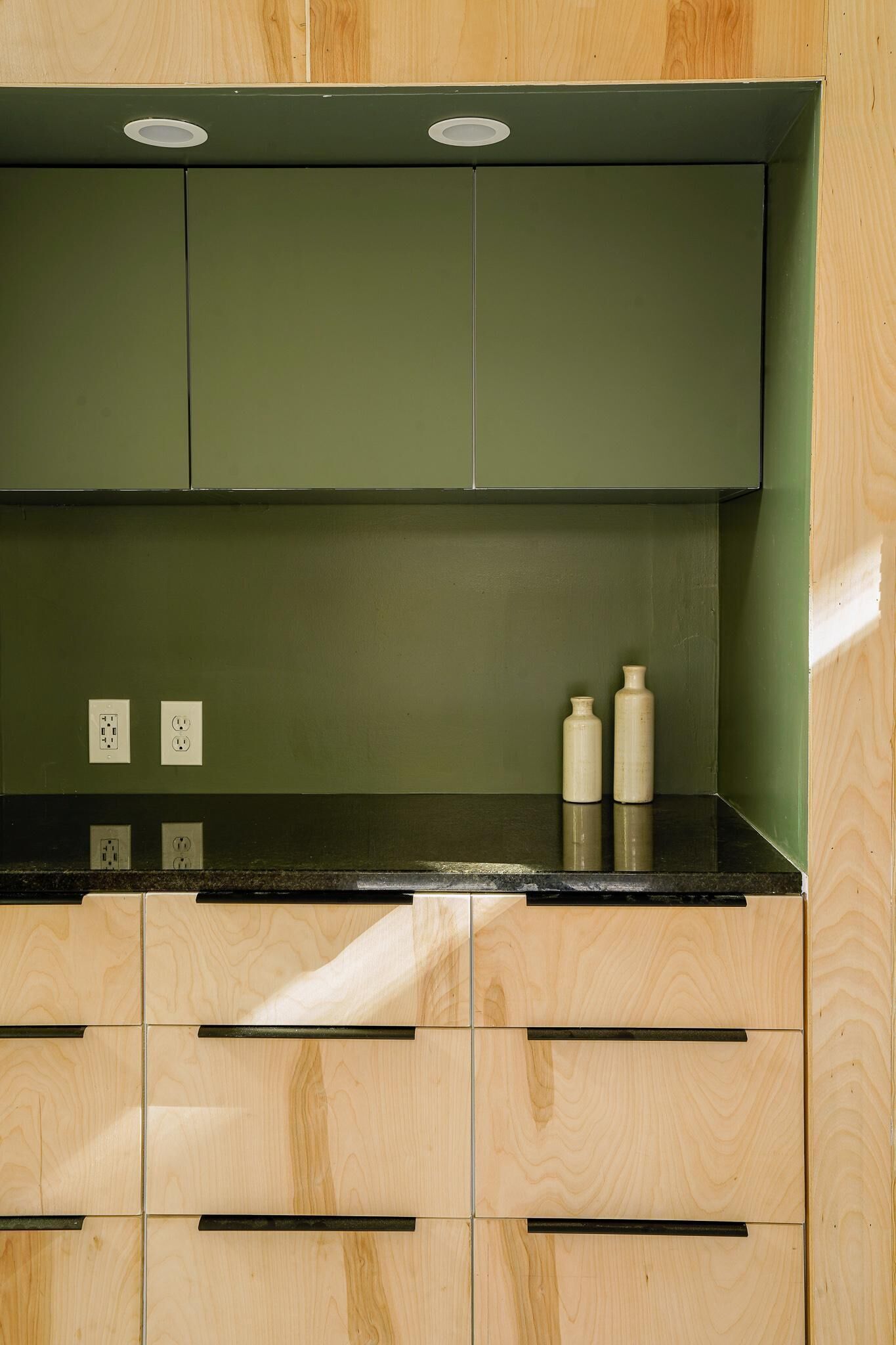 A kitchen with green cabinets, a black countertop, and two white bottles on the counter.