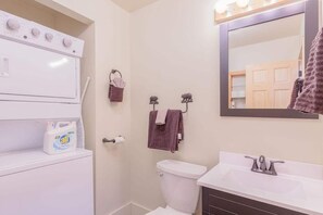 Ein Badezimmer mit Toilette, Waschbecken und Spiegel. Auf der Ablage liegen Handtücher und eine Flasche Flüssigseife.