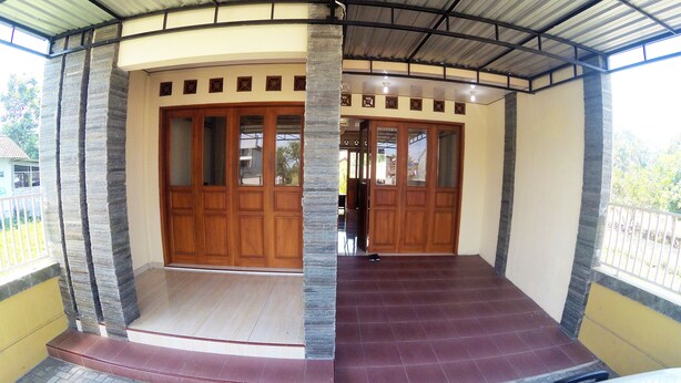 A covered entrance with a curved roof, wooden doors, and a tiled floor. - Next Trip Homestay Jogja (Jogja)