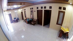 A spacious room with a tiled floor, a dining table with chairs, a television, and a small table with a yellow tablecloth. - Next Trip Homestay Jogja (Jogja)