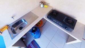 A small kitchen with a sink, stove, and tiled backsplash. - Next Trip Homestay Jogja (Jogja)