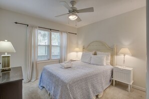Un dormitorio con una cama, dos mesitas de noche con lámparas, un ventilador de techo y una ventana con cortinas.