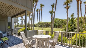 A wooden deck with outdoor furniture, a view of a golf course, and tall palm trees. - Kiawah Exclusives | 4973 Turtle Point Villa (Kiawah Island)