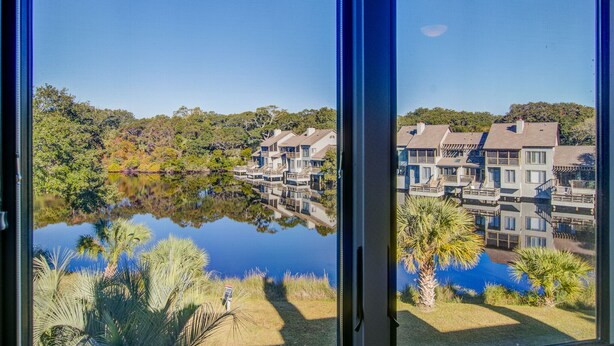 A view of a lakeside property with multiple buildings, a clear sky, and a reflection in the water.