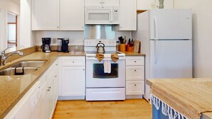 Une cuisine de taille réduite, dotée de meubles blancs, d’une cuisinière en acier inoxydable, d’un four à micro-ondes et d’un réfrigérateur.