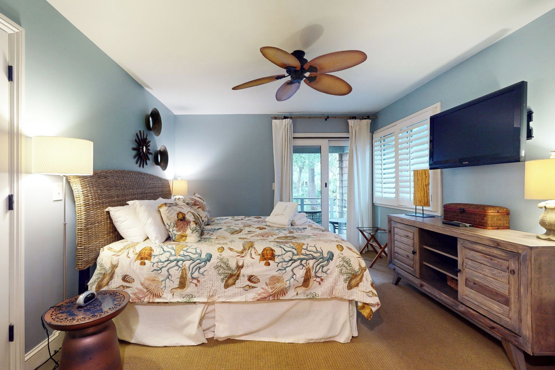 Un dormitorio con cama, ventilador de techo, cómoda, televisor y ventana con cortinas.