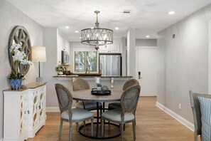 A dining area with a round table, four chairs, a chandelier, and a cabinet with decorative items. - Kiawah Exclusives | 4409 Windswept Villa (Kiawah Island)
