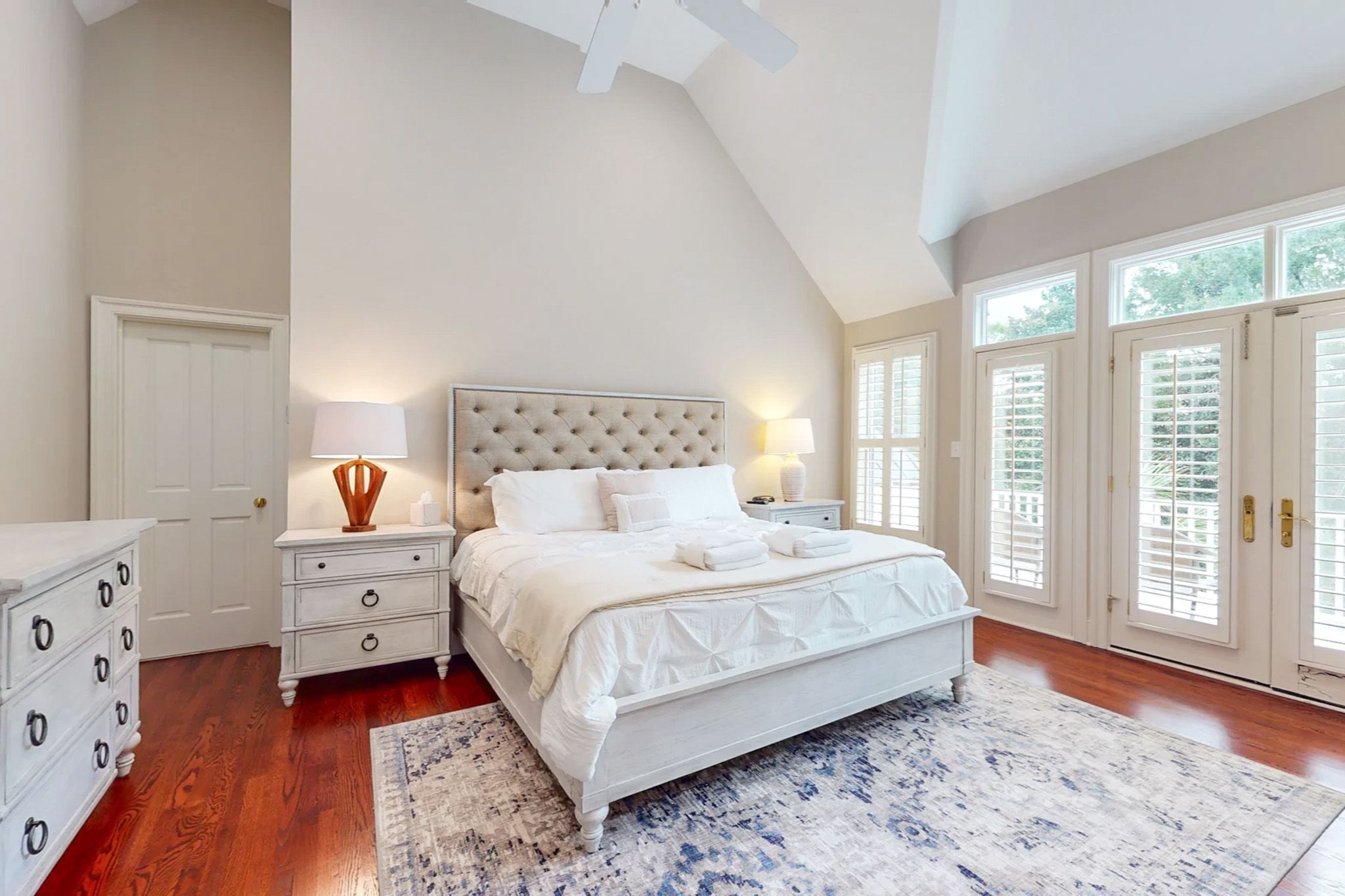 Une chambre à coucher avec un grand lit, une table de chevet, une commode et un ventilateur de plafond.