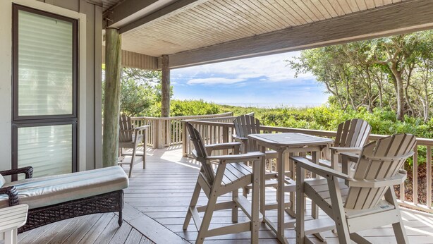 A covered outdoor deck with a table and chairs, overlooking a lush landscape.