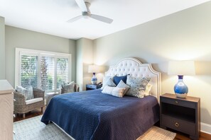 A bedroom with a large bed, two nightstands, a ceiling fan, and a window with blinds.