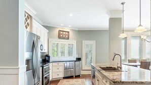 A modern kitchen with stainless steel appliances, a large island with a sink, and a dining area with wicker chairs.