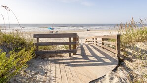 A wooden boardwalk leading to a beach with a bench and a blue umbrella.