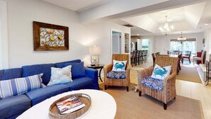 A living room with a blue sofa, wicker chairs, a white coffee table, and a painting on the wall.