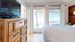 A bedroom with a TV on a wooden dresser, a bed, and a view of the outside.