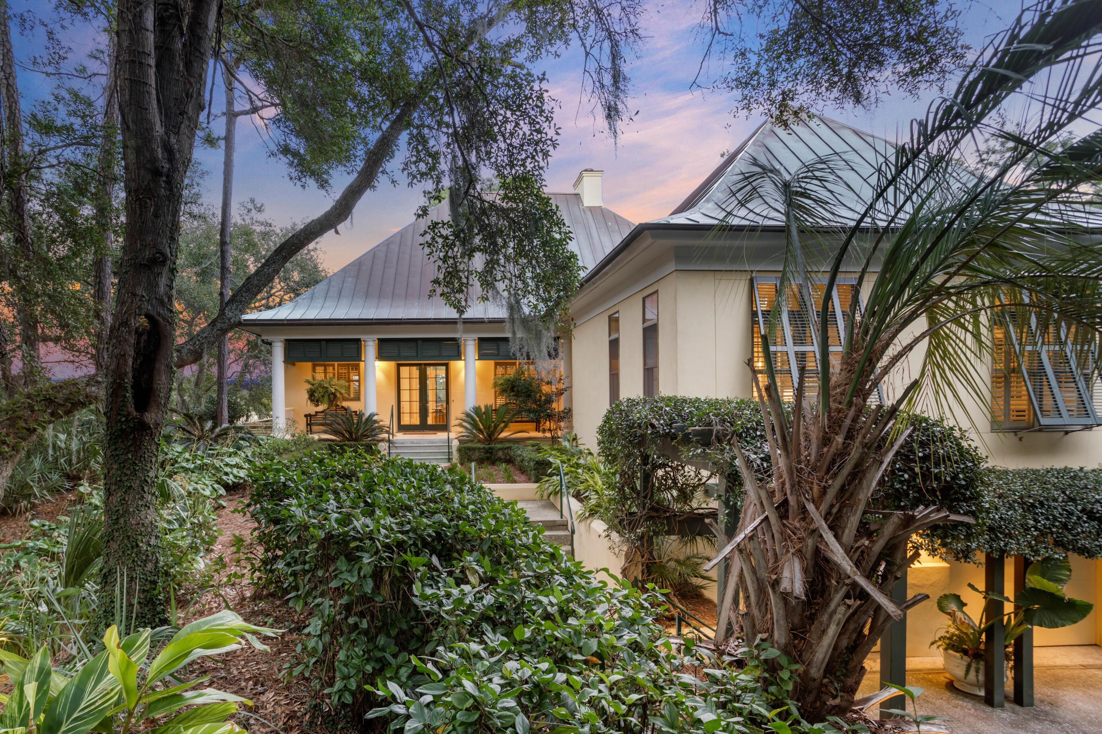 A house with a covered porch, surrounded by lush greenery and a large tree.