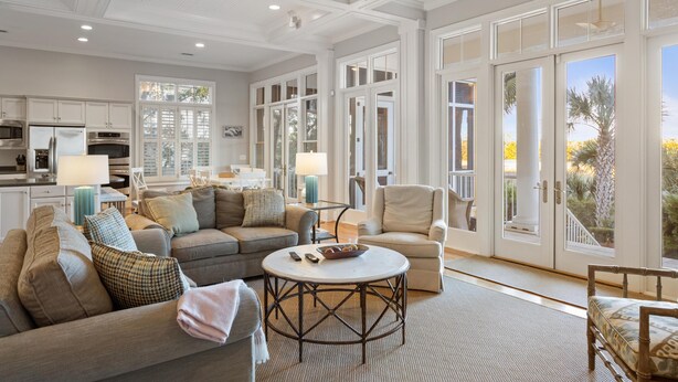 A spacious living room with a large sofa, a round coffee table, and a view of the outdoors through large sliding glass doors. - Kiawah Exclusives | 305 Ocean Oaks (Kiawah Island)