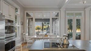 A kitchen with white cabinetry, a built-in oven, a stove, and a dining area with a table and chairs. - Kiawah Exclusives | 305 Ocean Oaks (Kiawah Island)