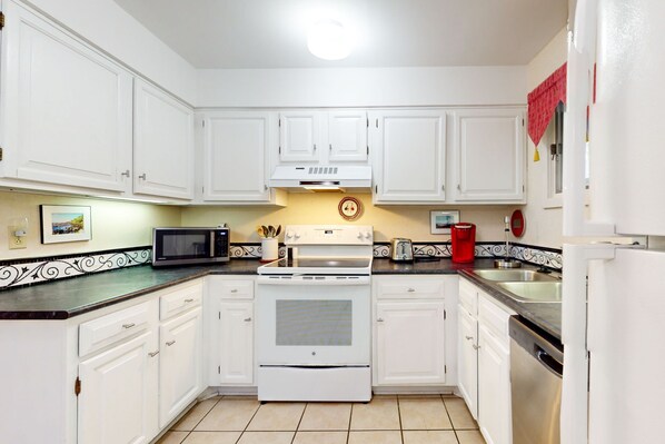 A kitchen with white cabinets, a microwave, a stove, a sink, and a red coffee maker.