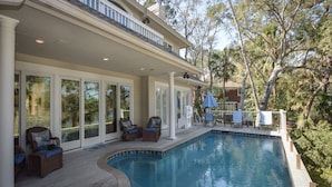 A poolside area with a covered patio, lounge chairs, and a swimming pool.