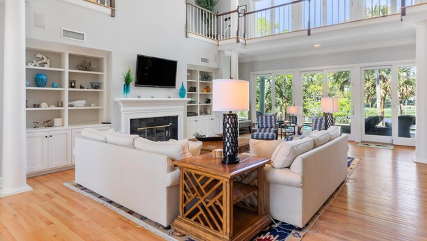 A spacious living room with a fireplace, white sofas, a TV, and a balcony with a railing.