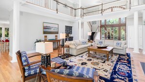 A spacious living room with a high ceiling, a staircase, and a view of the outdoors.