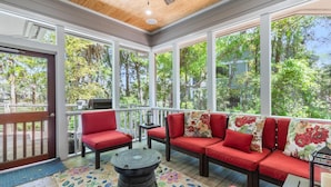 A covered porch with red seating, a wooden floor, and large windows offering a view of greenery.