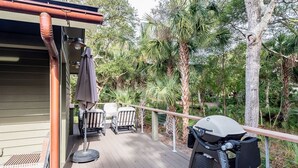 Eine Holzterrasse mit Gartenmöbeln, einem Grill und einer Pergola mit Tisch und Stühlen.