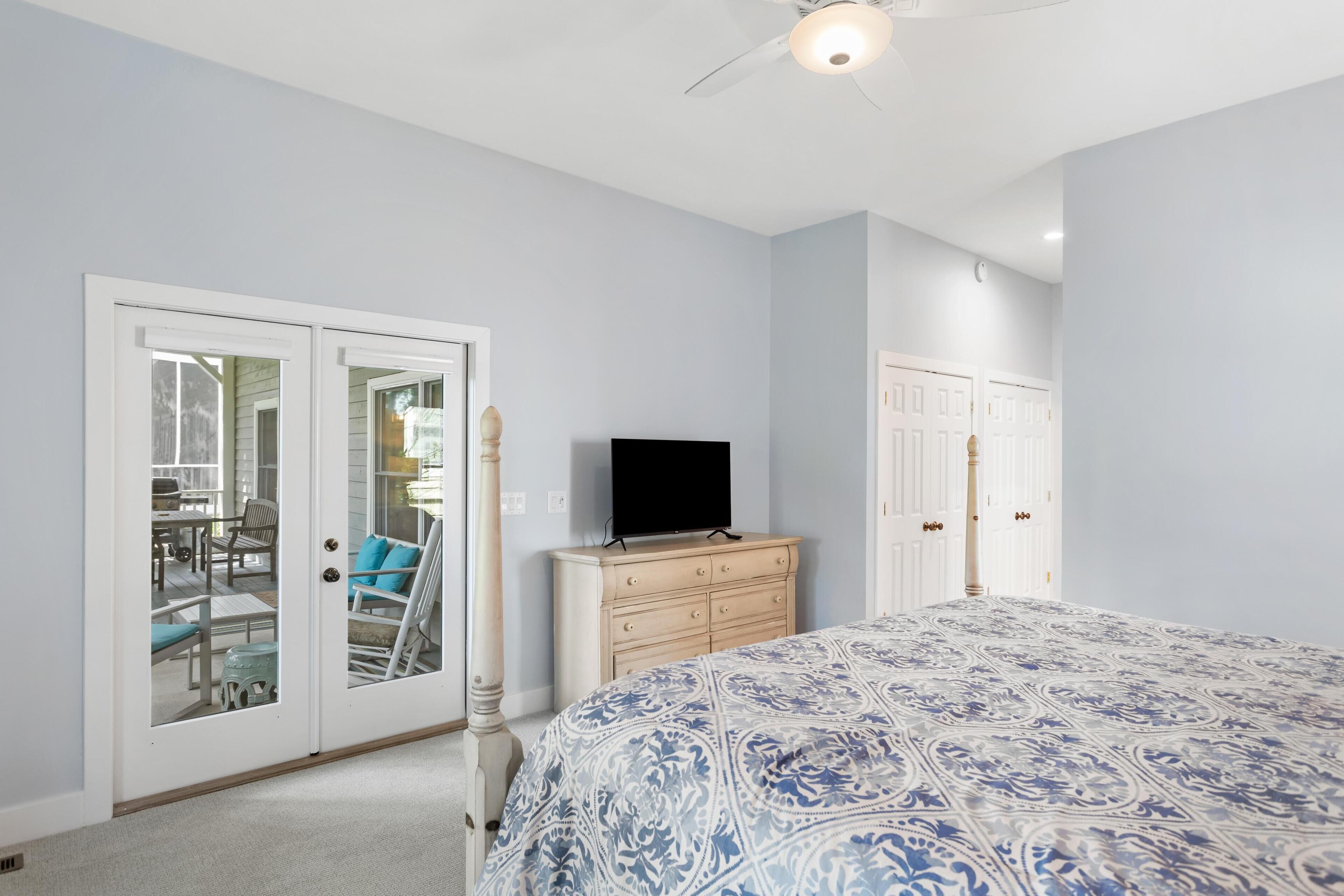 A bedroom with a bed, dresser, and a television. There are sliding glass doors leading to a patio area with outdoor furniture.