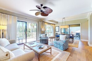 Uma sala de estar ampla com uma grande janela, um ventilador de teto e um espaço de refeições com mesa e cadeiras.