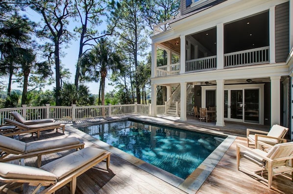 A two-story house with a swimming pool, outdoor furniture, and a deck.