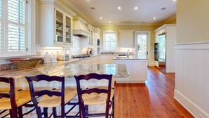 Una cocina amplia con armarios blancos, una isla grande con asientos y suelo de madera.