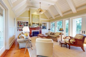 A spacious living room with a fireplace, comfortable seating, and large windows offering a view of the outdoors.