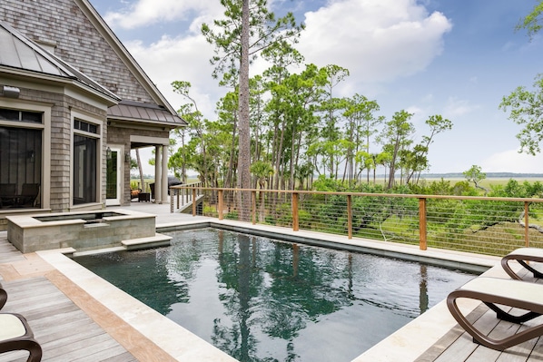 A swimming pool with a wooden deck, a covered patio, and a view of the surrounding landscape.