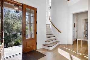 Staircase leads to an upper level, flanked by white walls and a glass door to an outdoor area.