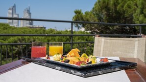 Ein Frühstücksbrett mit Obst und Saft auf einem Balkon mit Blick auf die Stadt.