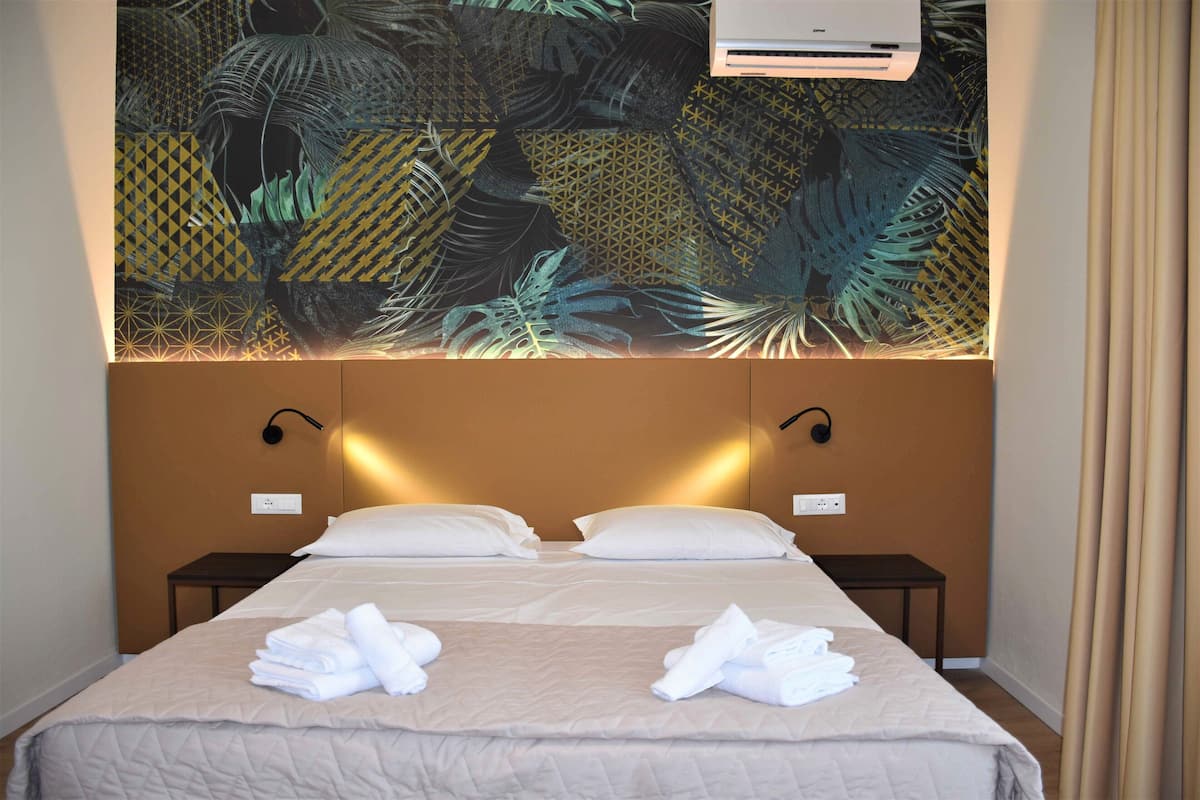 A hotel room with a large bed, two bedside tables, and a wall-mounted air conditioner.