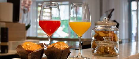 A kitchen counter with two glasses of juice, a jar of cookies, and two muffins on a plate.