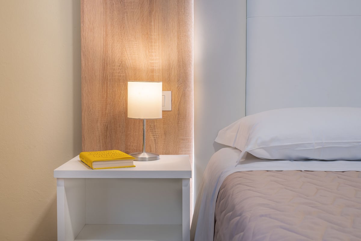A neatly made bed with white linens, a bedside table with a lamp, and a book.