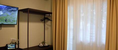 Habitación de hotel con televisión, escritorio con planta, perchero y cama con toalla.