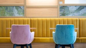 Ein modernes Interieur mit einer gelben Sitzbank und zwei Stühlen mit Holzarmlehnen.